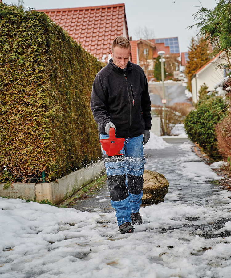 A man spreads salt in the snow using the Universal Spreader 